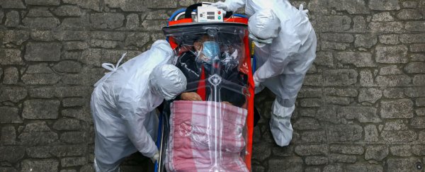 Two people in hazmat suits wheeling a patient on a stretcher