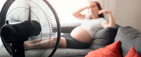 Pregnant woman sitting on couch in front of fan.