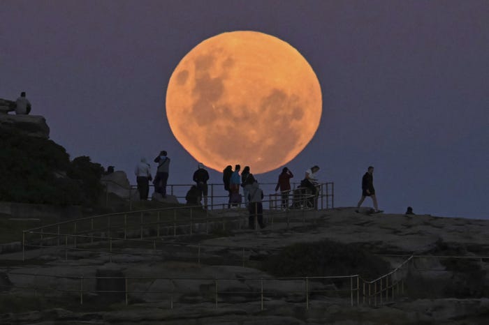 Gros plan de la pleine lune rose avec des silhouettes de personnes sur une falaise 