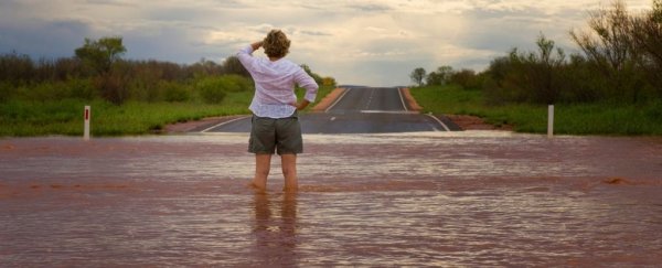 Woman wearing white shirt and short, standing knee-deep in flooded road.