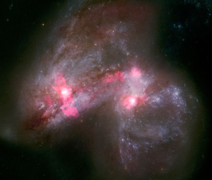 A luminous cloud with pink highlights shows two galaxies merging
