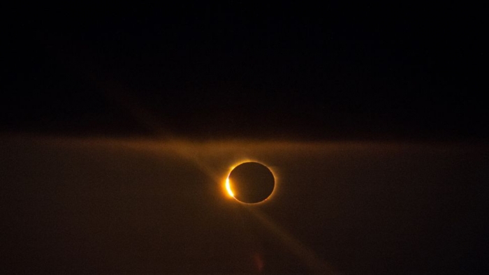 A black sky with a ring of orange light is brighter on one side.