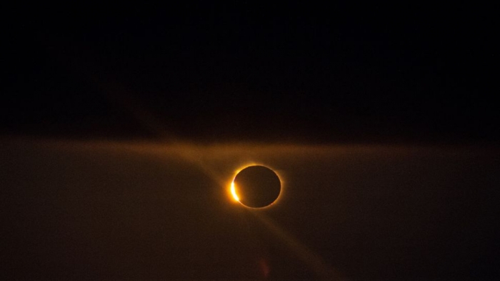 Black skies with ring of orange light brighter on one side.