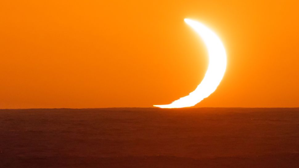 Large crescent of white light touching sea in red sky.