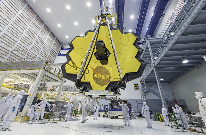 Golden telescope mirror above team of scientists in white suites.