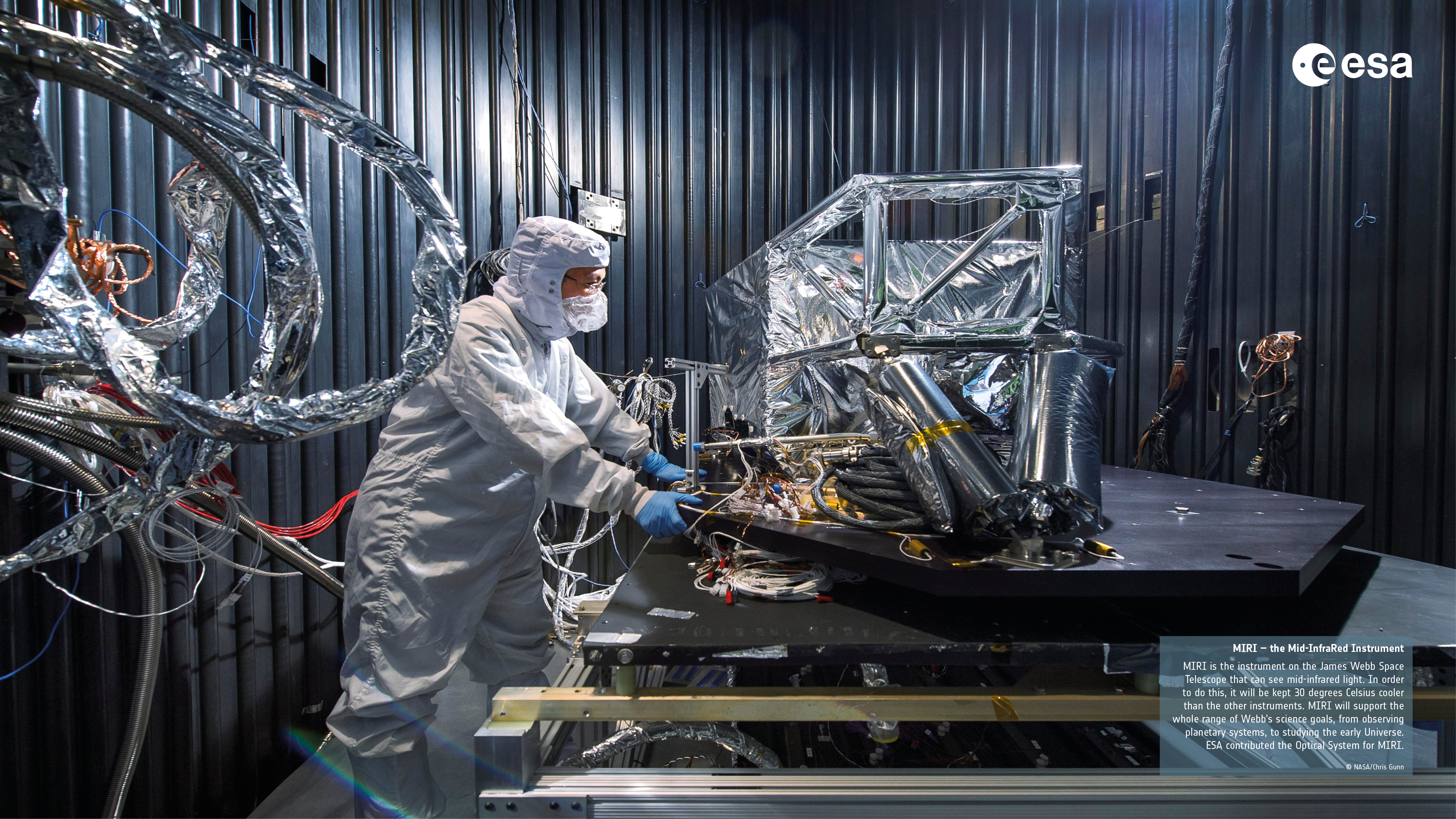 Suited person examining large foil covered device with cables.