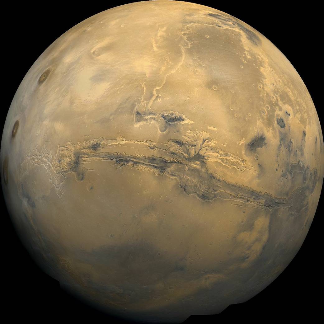 Globe of orange hued Mars showing a deep scar across much of the planet