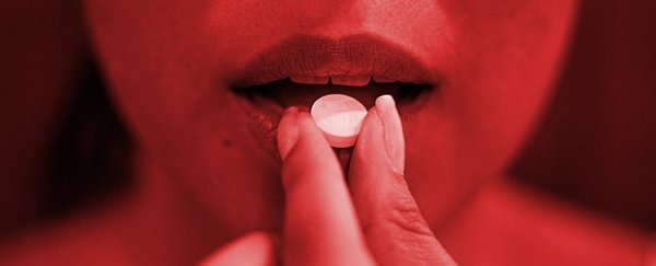 A hand holding a small white pill about to put into mouth