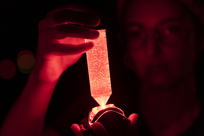 A person in glasses holding a glowing orange tube with small white specks in it