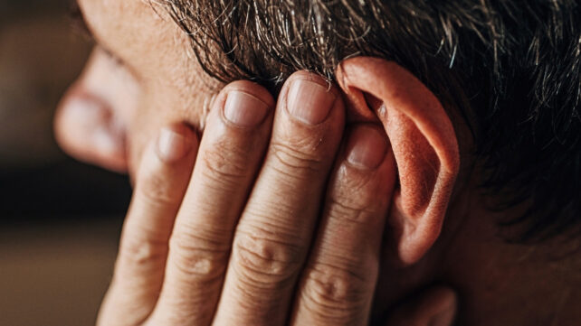 Close up of man's hand holding his ear, looking like he's in pain