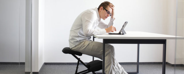 A man sits bent over a table, looking at a tablet.