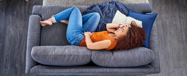 Woman curled up on sofa looking in pain