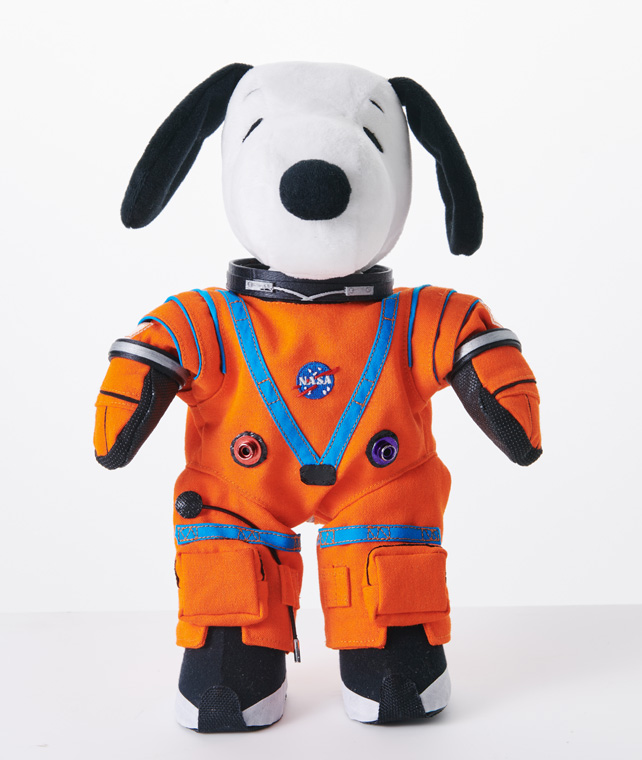 Snoopy, a black and white dog, wearing an orange NASA astronaut spacesuit.