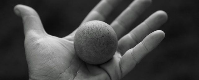 A black-and-white photo of a hand holding a rubber ball.