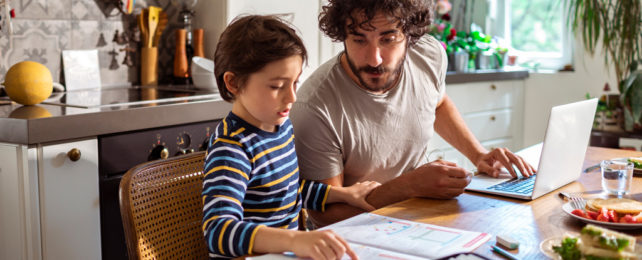 A man and a child do homework at a kitchen table.