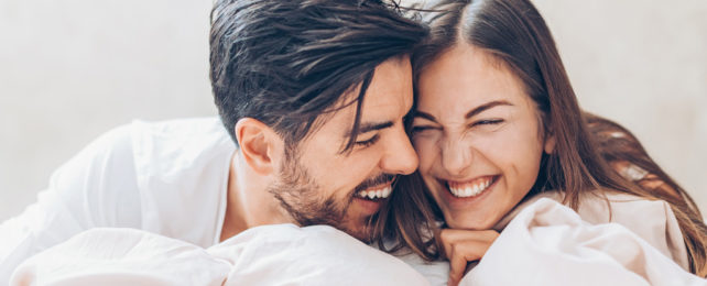 A man and a woman laughing together in bed.