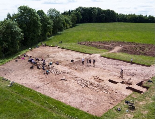 Excavación arqueológica de un lugar de entierro de la Edad de Piedra, rodeado de hierba verde y árboles.