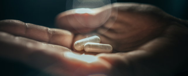 Two white pills sitting in the open palm of a person's hand, illuminating by light.