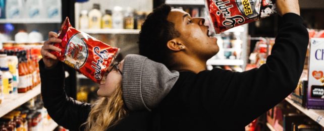 Couple Pouring Chips Into Mouths In Shop