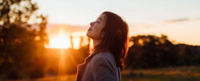 Girl with long hair silhouette by the sun at dusk, heading leaning back.