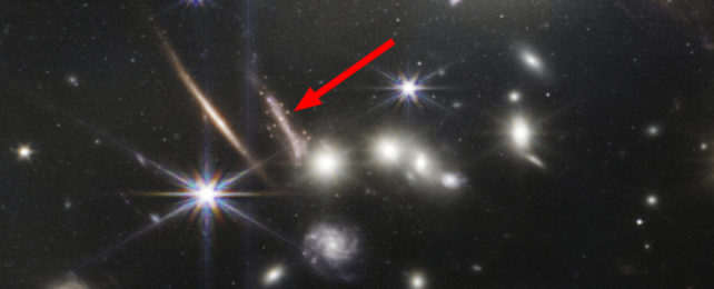 an arrow pointing to a zoomed image of the Sparkler galaxy, smeared and shimmering with dots of light around it