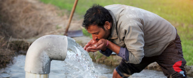 Man drinking water from a pump using his cupped hands.