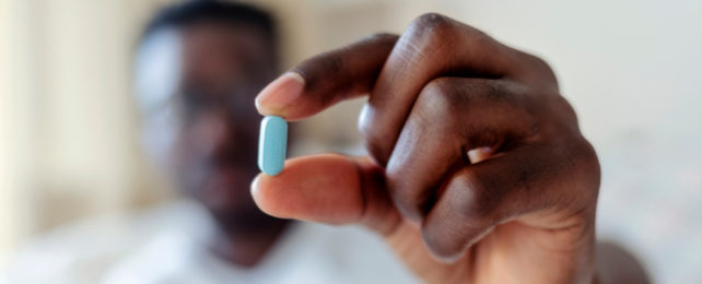 Man holding a blue pill between his thumb and forefinger.