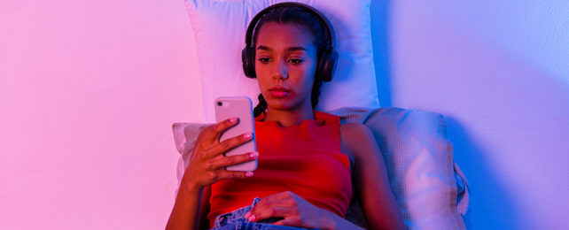 Teen girl sitting on her bed looking at a smart phone