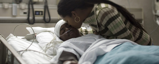 woman kissing unconscious patient in hospital bed