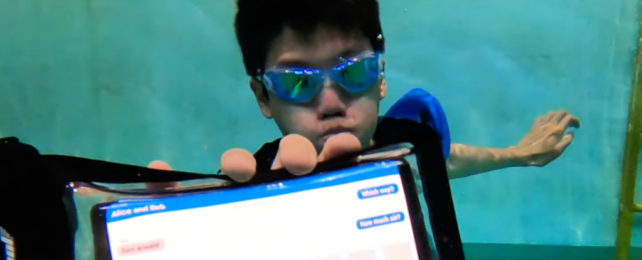 Man underwater in goggles holds up phone