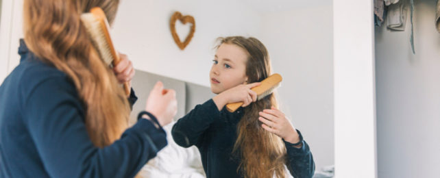 Young girl looking in mirror brushing her long, light brown hair.