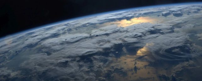 an image of earth taken from the international space station. the sun glints off the sea, and clouds populate the sky like islands