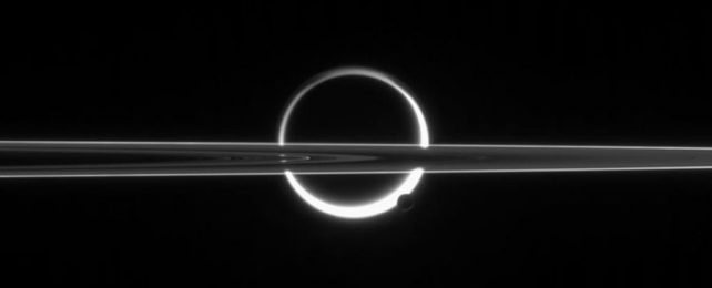 the rings of Saturn, cutting across the back-lit moon Titan, its atmosphere glowing in a ring around it, with enceladus in the foreground