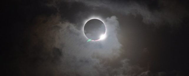 the dramatic ring of light of a total solar eclipse, with clouds drifing across the moon and sun