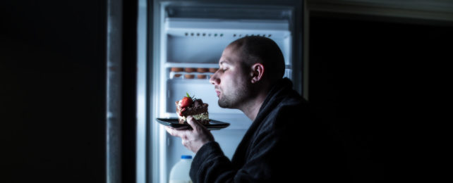 Man eating cake in front of a fridge