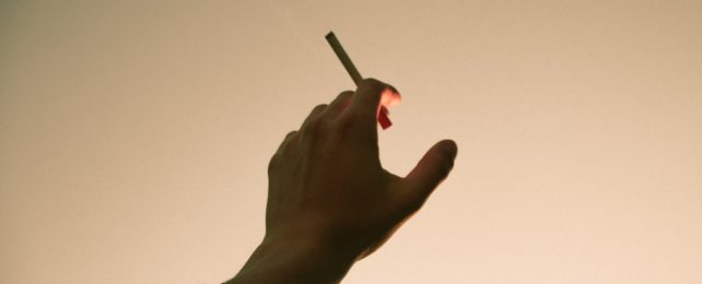 Hand Holds Cigarette Against Sky