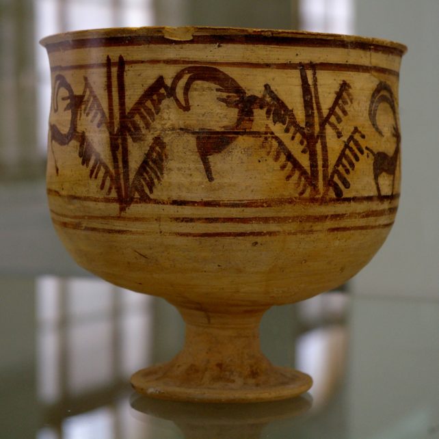 Earthenware vase bearing red sketches of a jumping goat and tree on display in a museum. 