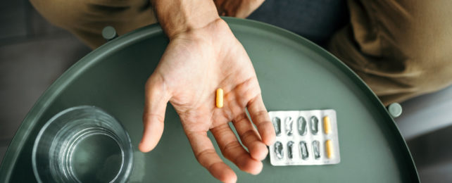 Man holding yellow capsule with packet and water nearby