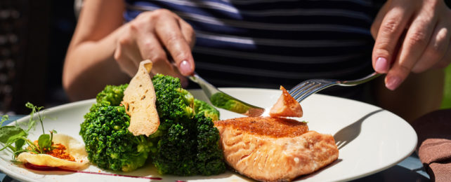 A person eating salmon and steamed broccoli.