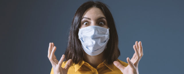 A stressed woman wearing a surgical mask.