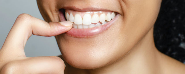 A woman smiling with a finger to her teeth.