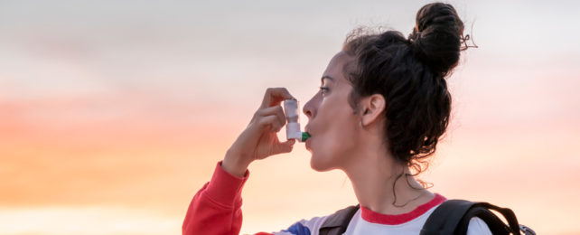 A woman uses an inhaler while hiking at sunrise.