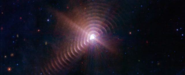 a glowing brilliant star is surrounded by concentric rings of purplish dust, expanding outwards into space