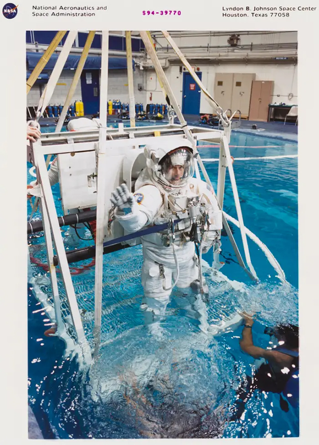 A student astronaut in a space suit is being lowered into a large pool
