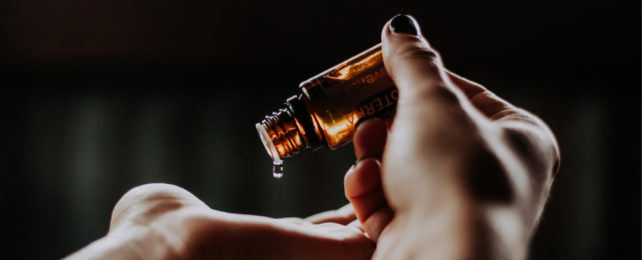 Close up image of a droplet of essential oil falling onto palm hand.