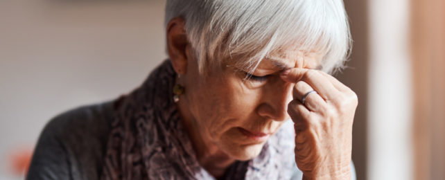 Grey haired woman clutching furrowed brow, in pain or discomfort.