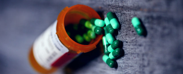 An orange prescription bottle with blue and green capsules spilling out of it.