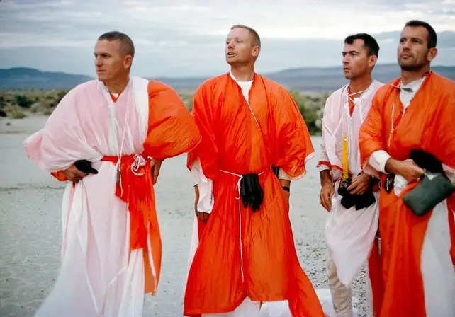 Four astronaut trainees in loose garments standing in a desert landscape