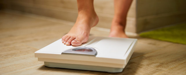 One bare foot tentatively standing on a set of bathroom scales