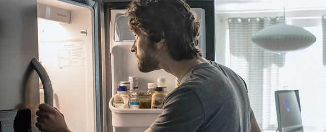 man opening fridge door and looking inside
